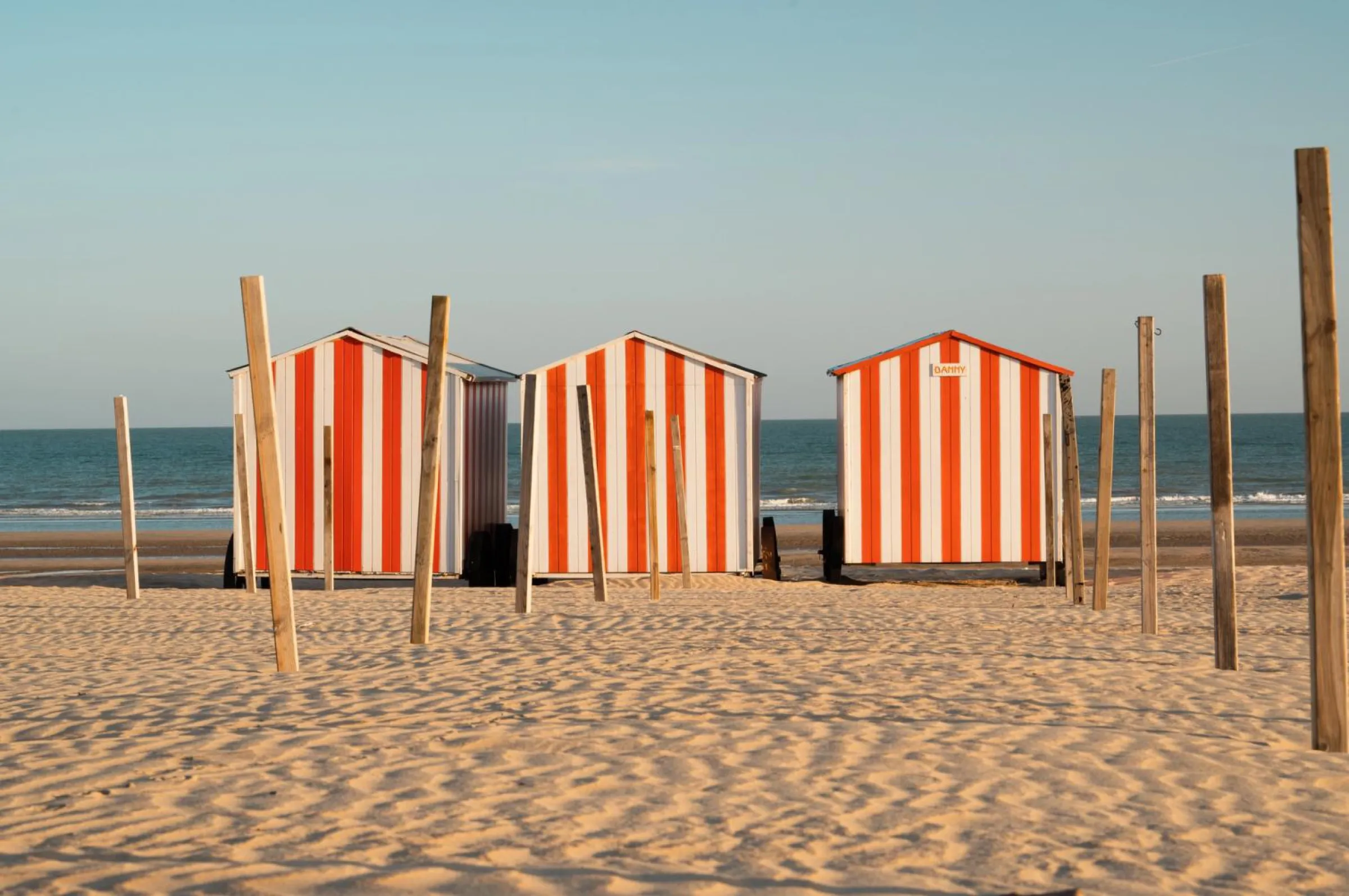 Cabines de plage rayées orange et blanc de La Panne, mer du Nord en fond, sable et digue en bord de mer