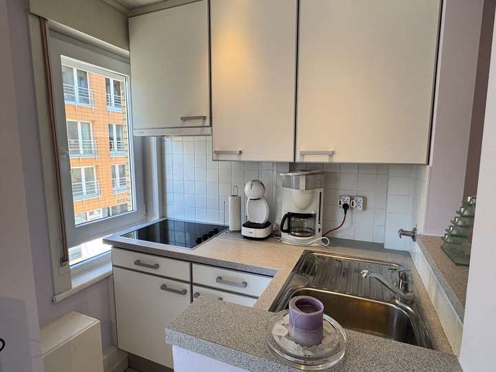 Cuisine équipée avec cafetière, plaques vitrocéramiques et vue sur la rue dans l’appartement de vacances Charm 202 à la mer